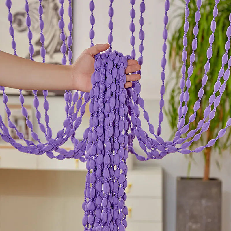 Purple beaded curtain with a hand holding it, indoor setting