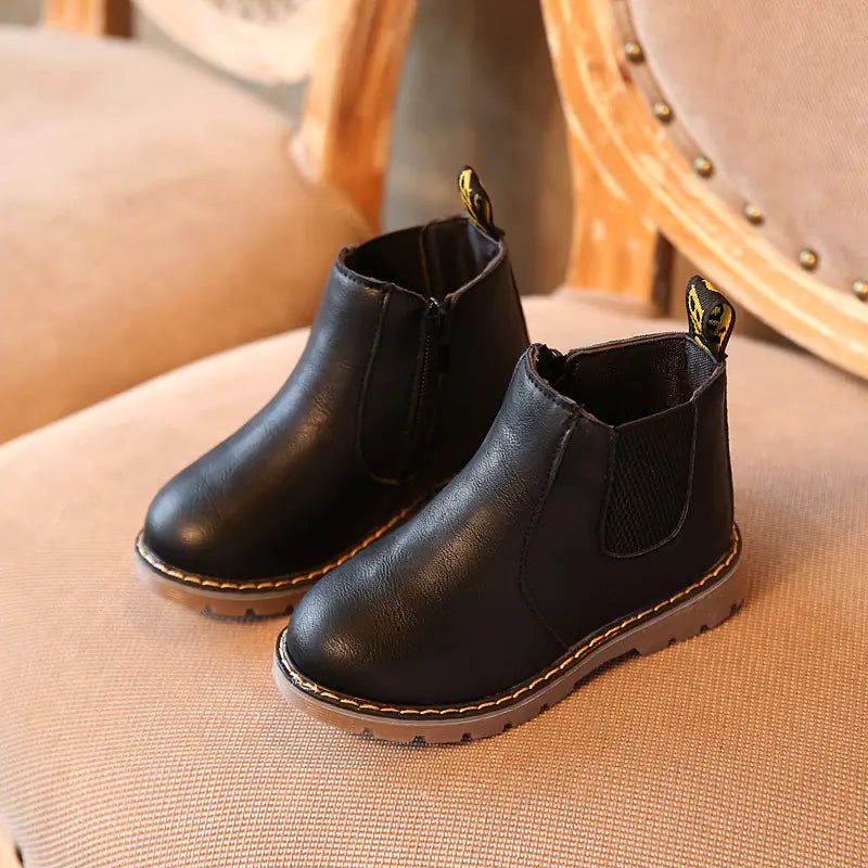 Pair of black leather boots on a beige cushioned surface.