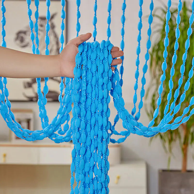 Blue beaded curtain held by a hand in a room with decor elements.