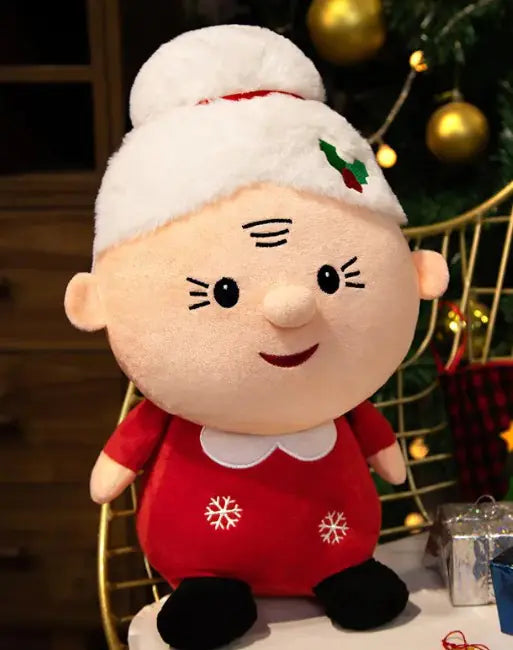 Plush toy resembling a character in a red outfit with white trim, sitting in front of a decorated Christmas tree.