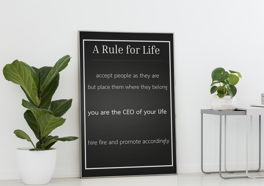 Framed 'A Rule for Life' poster on a white wall with plants and a small table.
