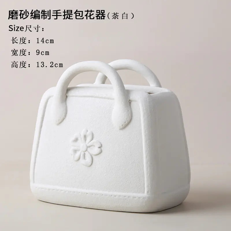 White ceramic handbag-shaped flower pot with floral design on a beige background